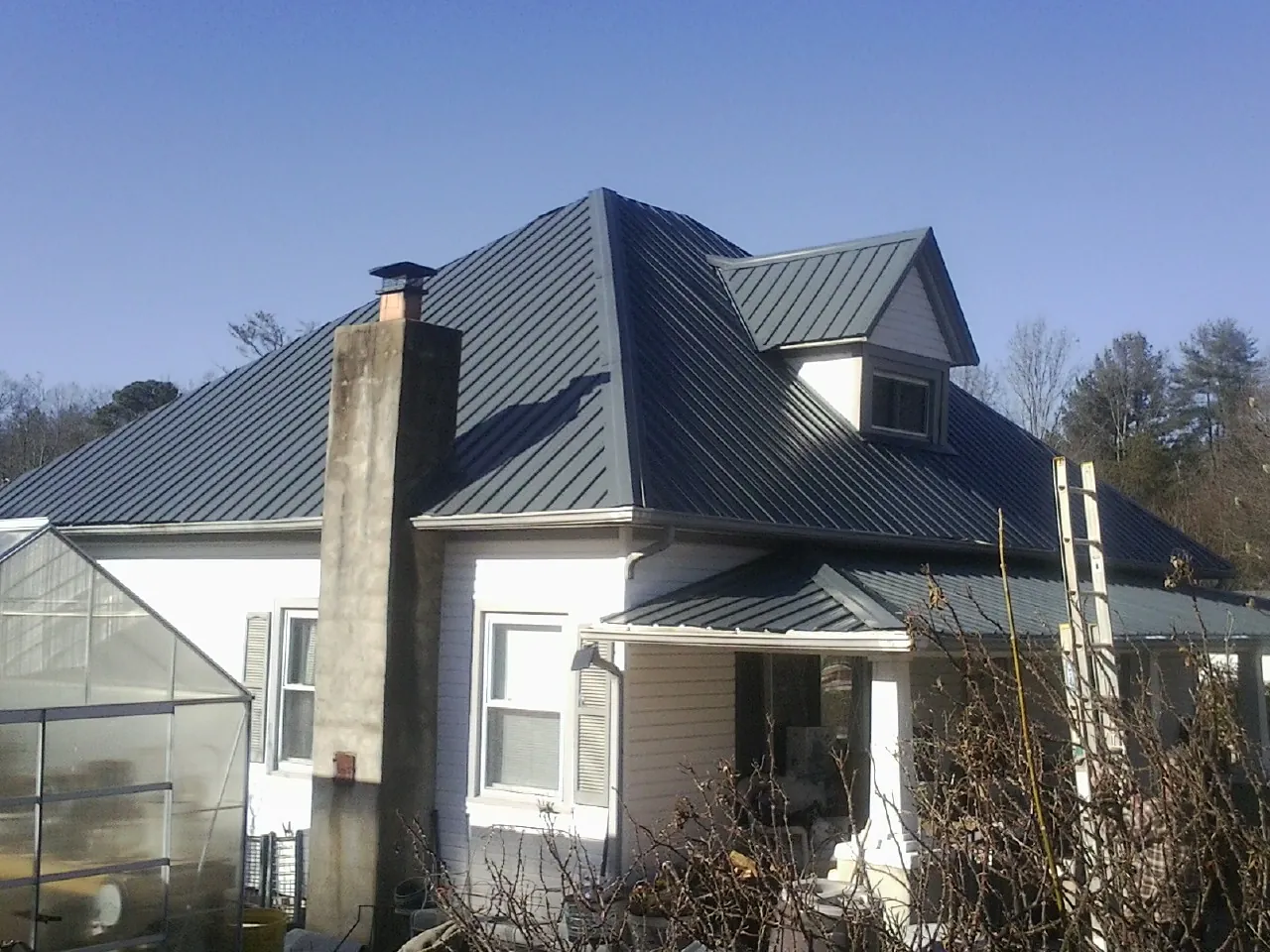 Dark blue standing seam metal roof on a white farmhouse with dormer — Slate & Tile Roof Repair by Roofing Brothers in Little Orleans