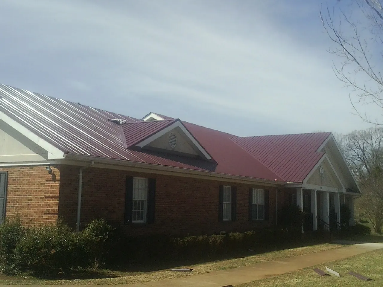 Red metal roof with gabled entries on a long brick building, from a Hail Damage Roof Repair job in Little Orleans
