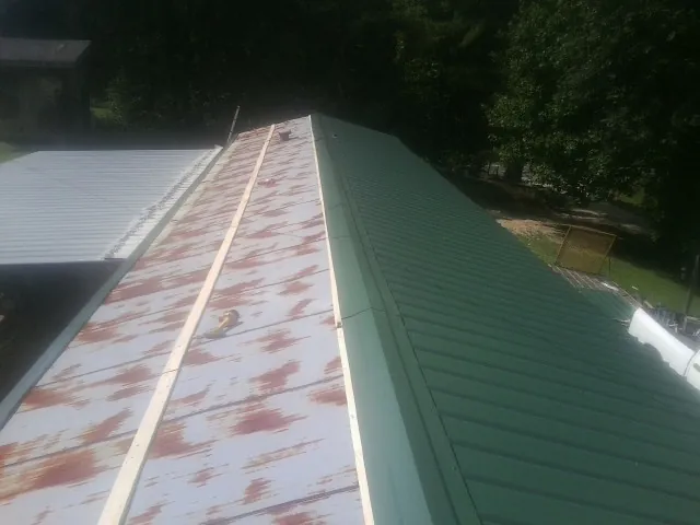 Old rusted panels beside newly installed green metal roofing — Wind Damage Roof Repair by Roofing Brothers in Little Orleans