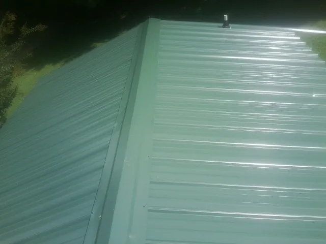 New green metal panels meeting at the ridge of a roof — Flat Roof Repair work by our crew in Little Orleans