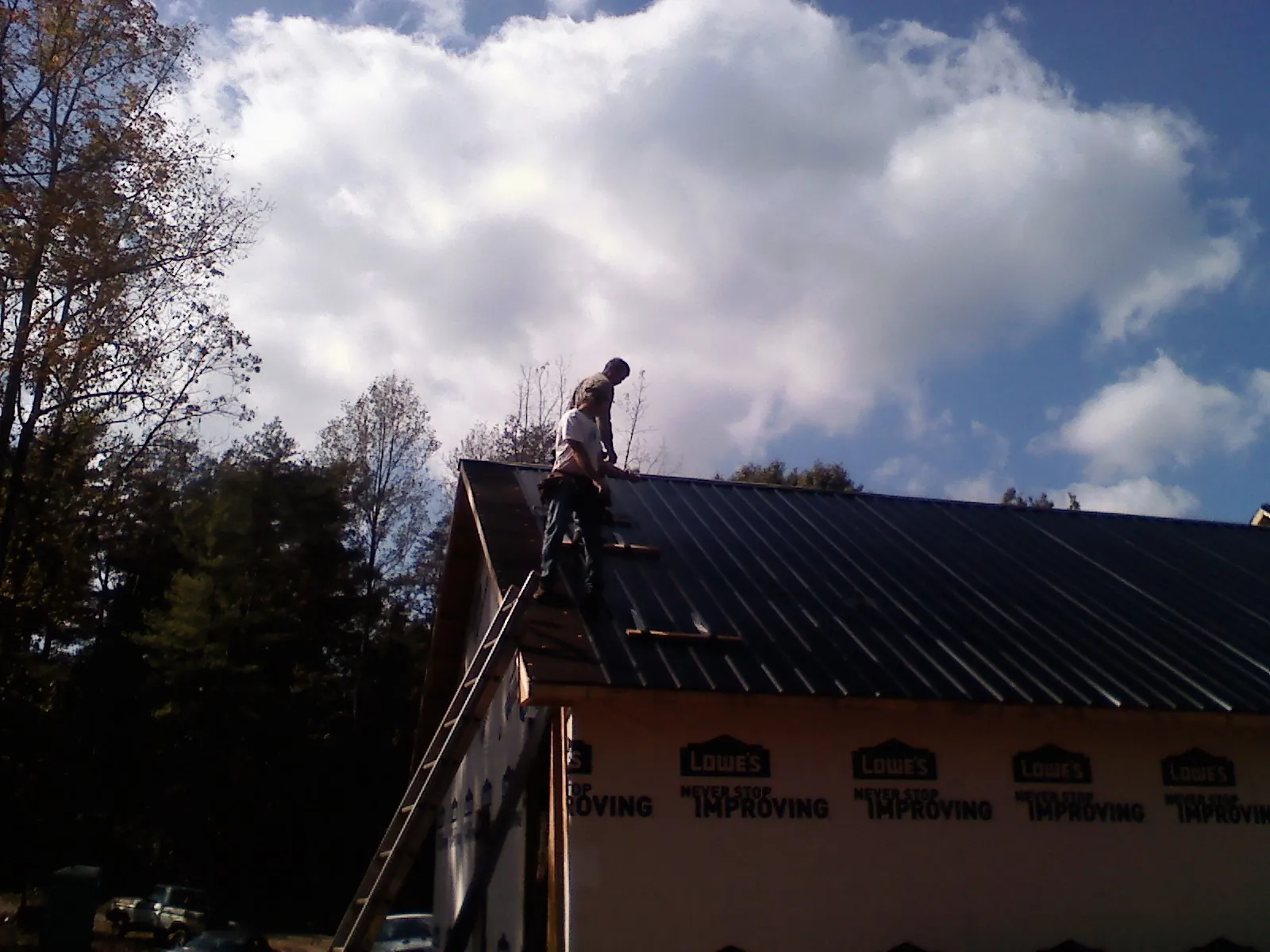 Roofer fastening dark metal panels high against a cloudy sky, from a Roof Inspection job in Little Orleans