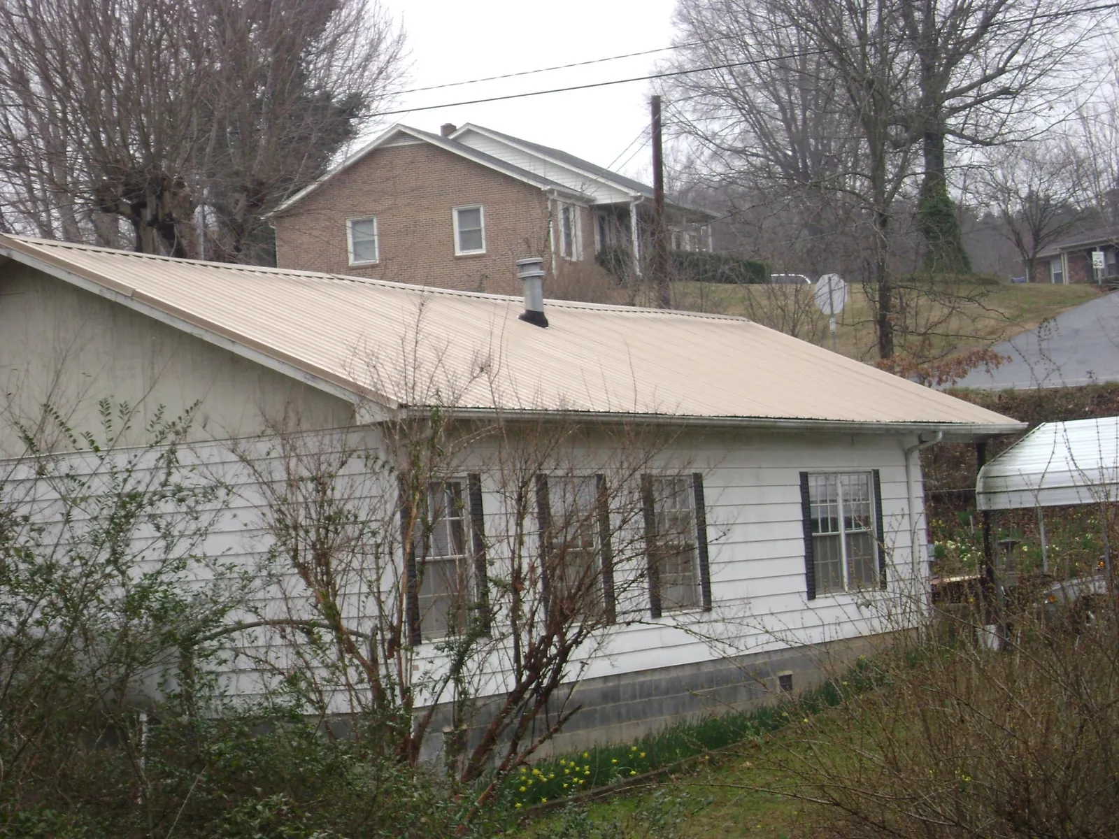 Tan metal roof on a white sided house set into a hillside — Commercial Roofing by Roofing Brothers in Little Orleans