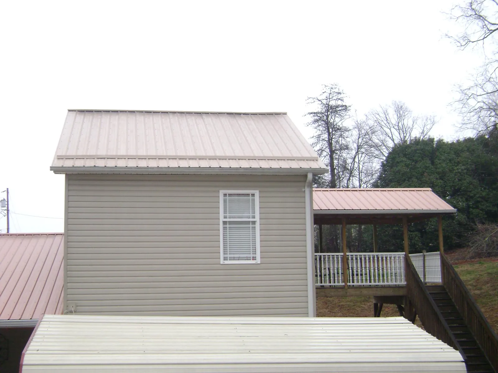 Tan metal roofs on a two story addition and attached porch, from a Roof Replacement job in Little Orleans